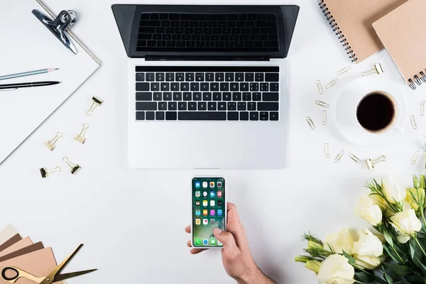 KYIV, UKRAINE - MAY 11, 2019: cropped view of man holding smartphone with home page on screen at workplace — Stock Photo