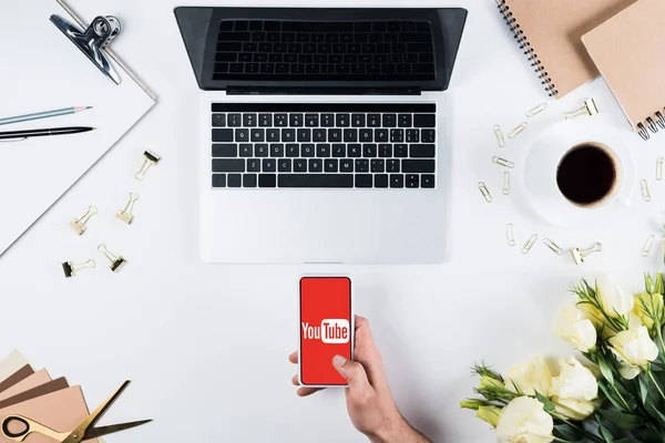 KYIV, UKRAINE - MAY 11, 2019: cropped view of man holding smartphone with youtube app on screen at workplace — Stock Photo