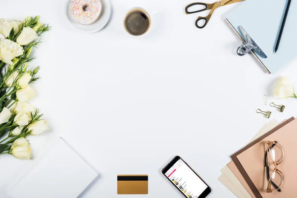 KYIV, UKRAINE - MAY 11, 2019: top view of cup of coffee, doughnut, credit card, flowers, glasses, scissors, clipboard and smartphone with apple music app on screen on white — Stock Photo