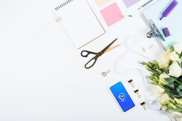 KYIV, UKRAINE - MAY 11, 2019: top view of flowers, scissors, notebook, clipboard and smartphone with shazam app on screen on white — Stock Photo