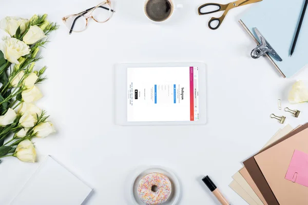 KYIV, UKRAINE - MAY 11, 2019: top view of cup of coffee, doughnut, flowers, glasses, book, papers, clipboard and digital tablet with instagram app on screen on white — Stock Photo