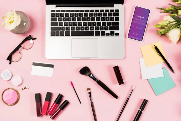 KYIV, UKRAINE - MAY 11, 2019: top view of laptop, smartphone with instagram app on screen, flowers, credit card and decorative cosmetics on pink — Stock Photo