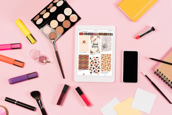 KYIV, UKRAINE - MAY 11, 2019: top view of digital tablet with pinterest app on screen, smartphone with blank screen, highlighters and decorative cosmetics on pink — Stock Photo