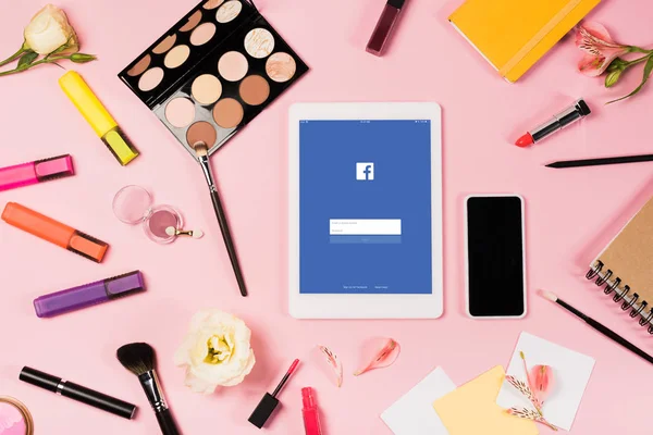 Kyiv, Ukraine - 11. Mai 2019: Draufsicht auf digitales Tablet mit Facebook-App auf dem Bildschirm, Smartphone mit leerem Bildschirm, Blumen, Textmarker und dekorative Kosmetik auf rosa — Stockfoto