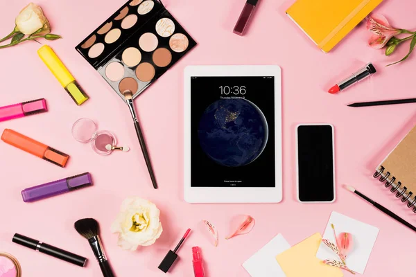 KYIV, UCRAINA - 11 MAGGIO 2019: vista dall'alto del tablet digitale con schermo di blocco, smartphone con schermo bianco, fiori, evidenziatori e cosmetici decorativi su rosa — Foto stock