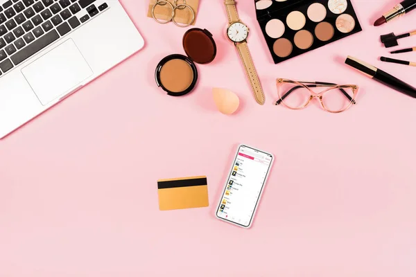 KYIV, UKRAINE - MAY 11, 2019: top view of laptop, decorative cosmetics, glasses, wristwatch, credit card and smartphone with apple music app on screen on pink — Stock Photo