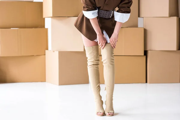 Vue recadrée de fille touchant bottes tout en se tenant près de boîtes sur blanc — Photo de stock