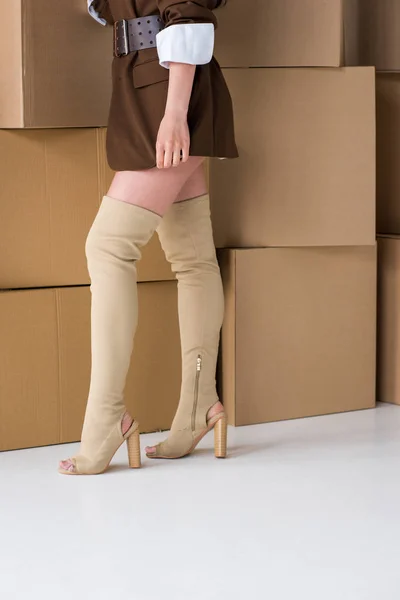 Cropped view of girl standing in boots near boxes on white — Stock Photo