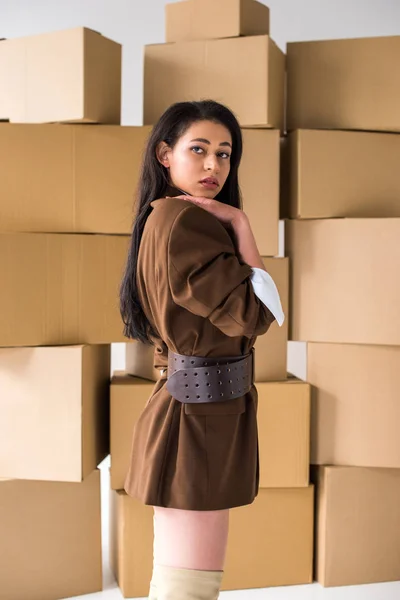 Atractiva chica afroamericana mirando a la cámara cerca de cajas en blanco - foto de stock