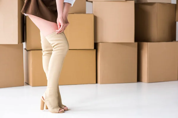Vista ritagliata di ragazza in piedi e toccare stivali vicino scatole su bianco — Foto stock