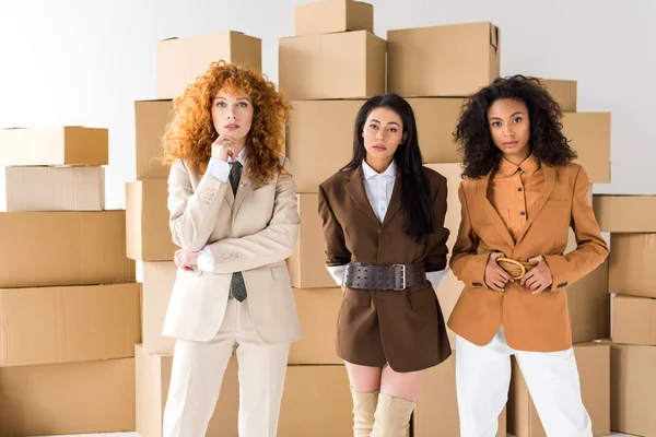 Redhead girl standing near african american young women and boxes on white — Stock Photo