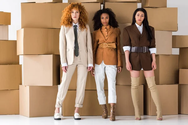 Attractive redhead girl standing near stylish african american young women and boxes on white — Stock Photo