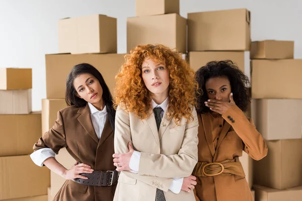 Attractive redhead girl looking at camera with stylish african american young women near boxes on white — Stock Photo