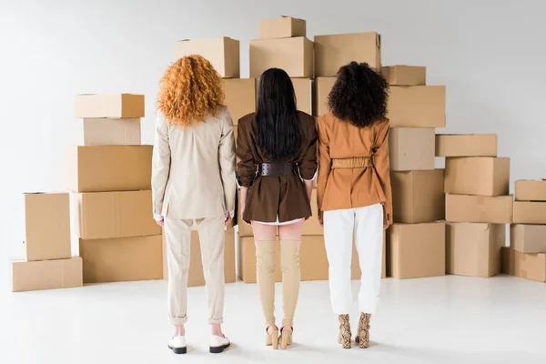 Вид сзади рыжеволосой девушки, стоящей со стильными африканскими женщинами рядом с коробками на белом — стоковое фото