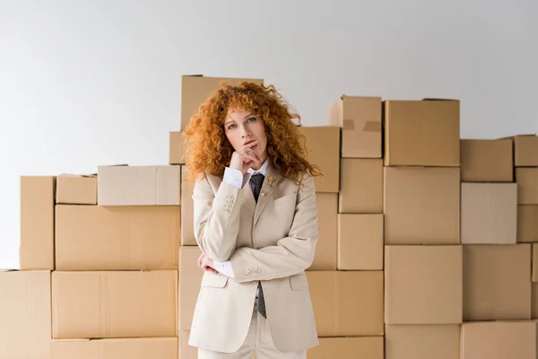 Attractive curly redhead girl looking at camera near boxes on white — Stock Photo
