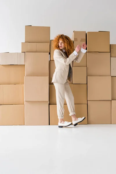 Atractiva pelirroja rizada de pie cerca de cajas en blanco - foto de stock