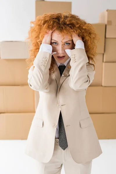 Attractive curly redhead girl touching hair near boxes on white — Stock Photo