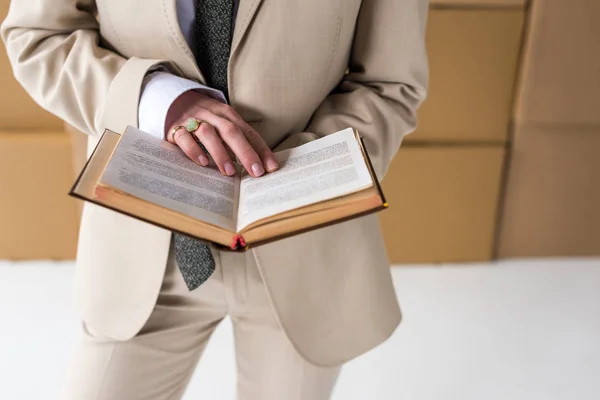 Vue recadrée de la femme en tenue formelle livre près des boîtes sur blanc — Photo de stock