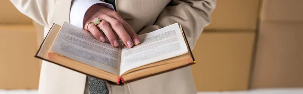 Panoramic shot of woman in formal wear holding book near boxes — Stock Photo