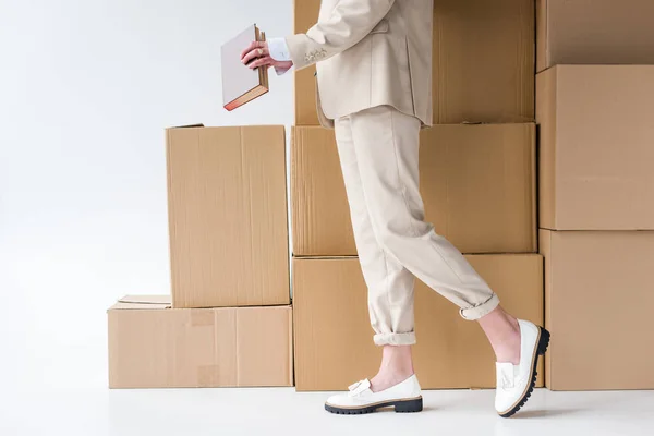 Cropped view of woman in formal wear standing near boxes and holding book on white — Stock Photo