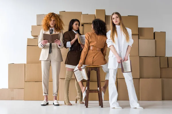 Attraktive multikulturelle Mädchen mit Büchern in der Nähe von Schachteln auf weiß — Stockfoto