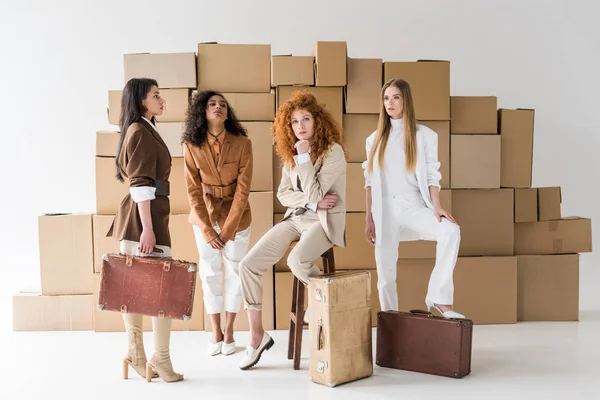 Chicas multiculturales atractivas de pie con maletas cerca de cajas en blanco - foto de stock