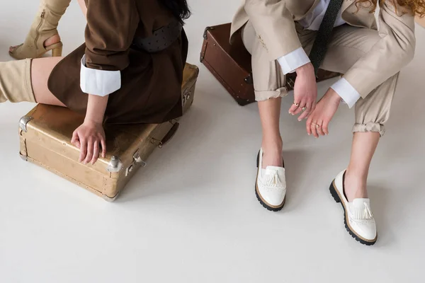 Vista recortada de las mujeres jóvenes sentadas en bolsas de viaje en blanco - foto de stock