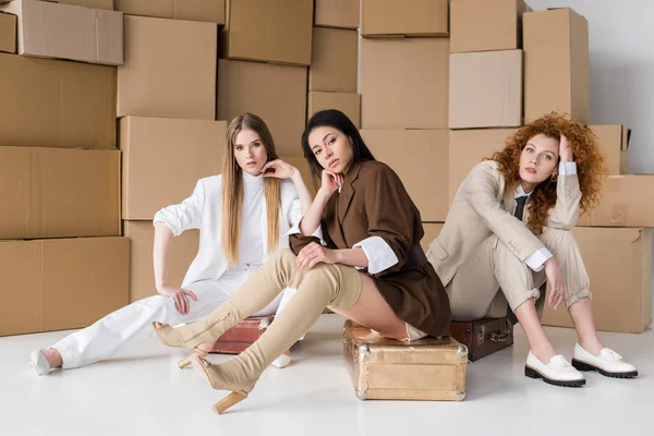 Chica afroamericana sentada en el equipaje cerca de las mujeres y cajas en blanco - foto de stock