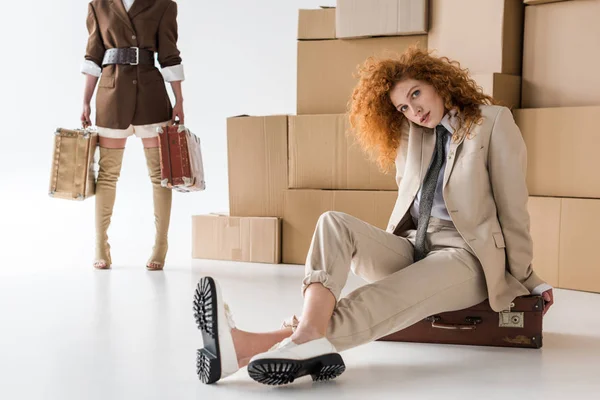 Cropped view of woman standing with travel bags near redhead girl sitting on white — Stock Photo