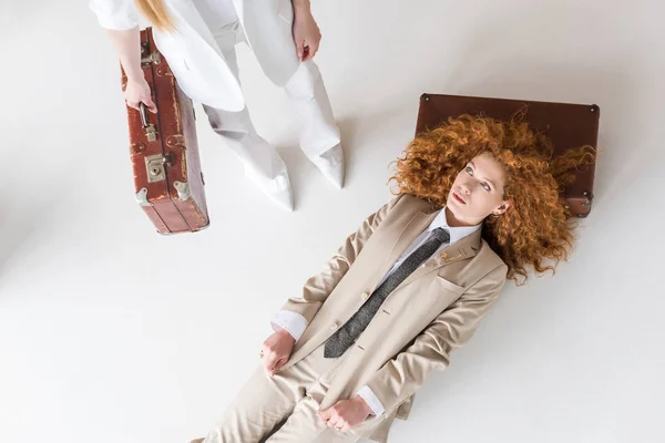 Top view of redhead woman lying near girl standing with suitcase on white — стоковое фото