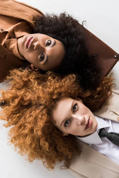 Top view of redhead girl lying on suitcase with african american curly woman isolated on white e — Stock Photo