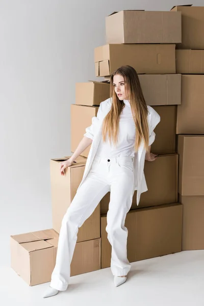 Attractive blonde young woman posing near carton boxes on white — Stock Photo