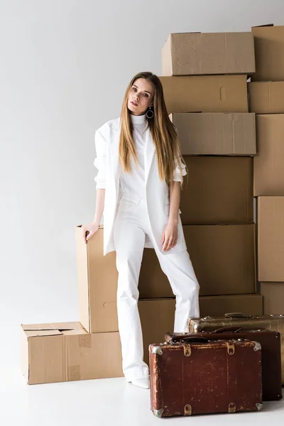 Attraktive blonde junge Frau posiert in der Nähe von Koffern und Kartons auf weiß — Stockfoto