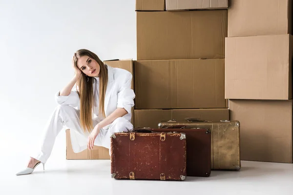 Jolie femme blonde posant près de valises et boîtes en carton sur blanc — Photo de stock