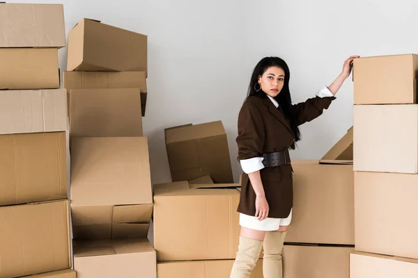 Attractive african american woman standing near carton boxes and looking at camera on white — Stock Photo