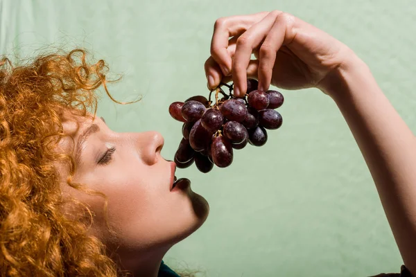 Красива кучерява руда жінка тримає солодкий виноград на зеленому — стокове фото