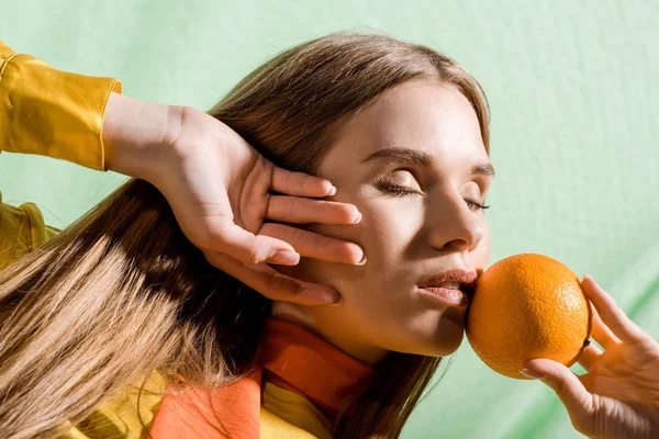 Beautiful blonde woman with closed eyes holding orange on green — Stock Photo