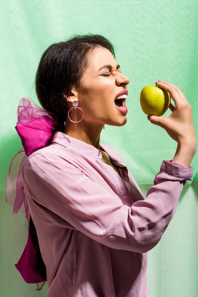 Brunette african american girl eating green apple on green — Stock Photo