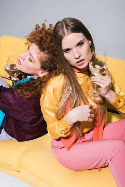 Vista aérea de chica pelirroja cerca de mujer rubia con copa de champán sentado en sofá amarillo en blanco — Stock Photo