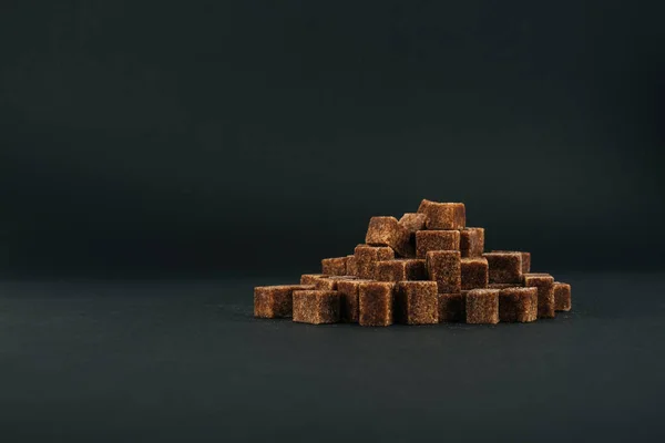 Купа нерафінованих коричневих кубиків цукру на чорному тлі з копіювальним простором — стокове фото