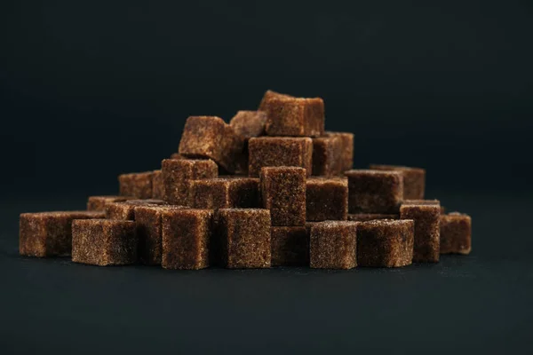 Pile of unrefined brown sugar cubes on black background — Stock Photo