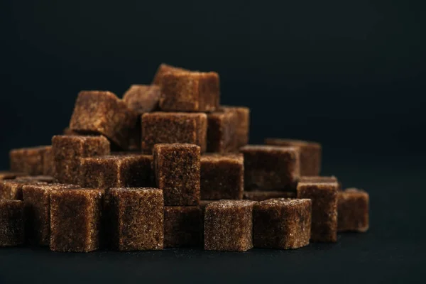 Pila de dulces cubos de azúcar moreno sin refinar sobre fondo negro - foto de stock