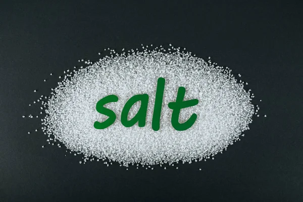 Top view of green paper cut word salt on salt crystals on black background — Stock Photo