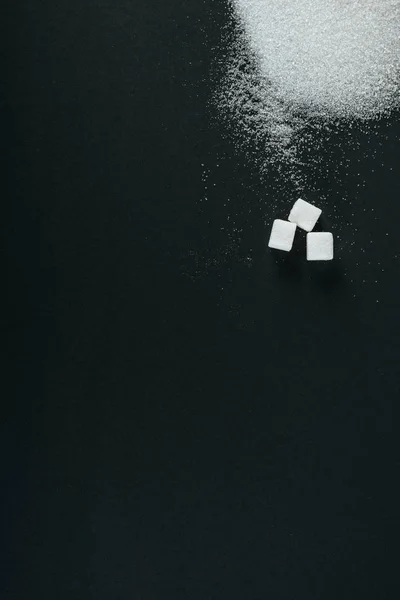 Top view of white sugar crystals and cubes on black background with copy space — Stock Photo