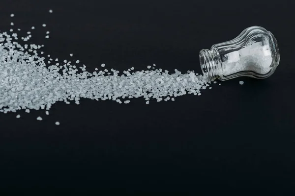 Top view of salt shaker near sprinkled salt crystals on black background — Stock Photo