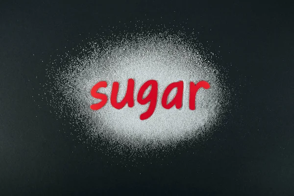 Верхний вид кристаллов белого сахара с красной бумагой сократить слово сахар на черном фоне — стоковое фото