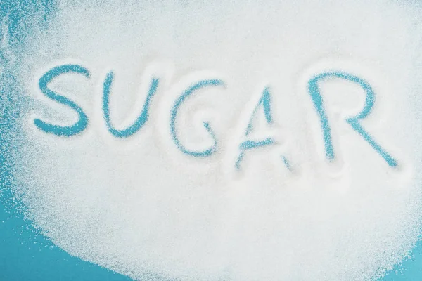 Top view of word sugar made on sprinkled white sugar crystals on blue surface — Stock Photo