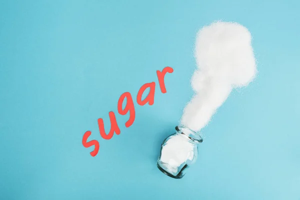 Top view of red paper cut word sugar near sugar crystals and glass jar on blue background — Stock Photo