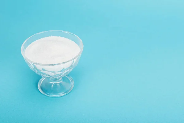 Glass bowl with white granulated sugar on blue background with copy space — Stock Photo