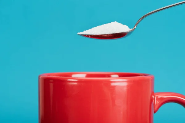 Teaspoonful of granulated sugar near red cup isolated on blue — Stock Photo